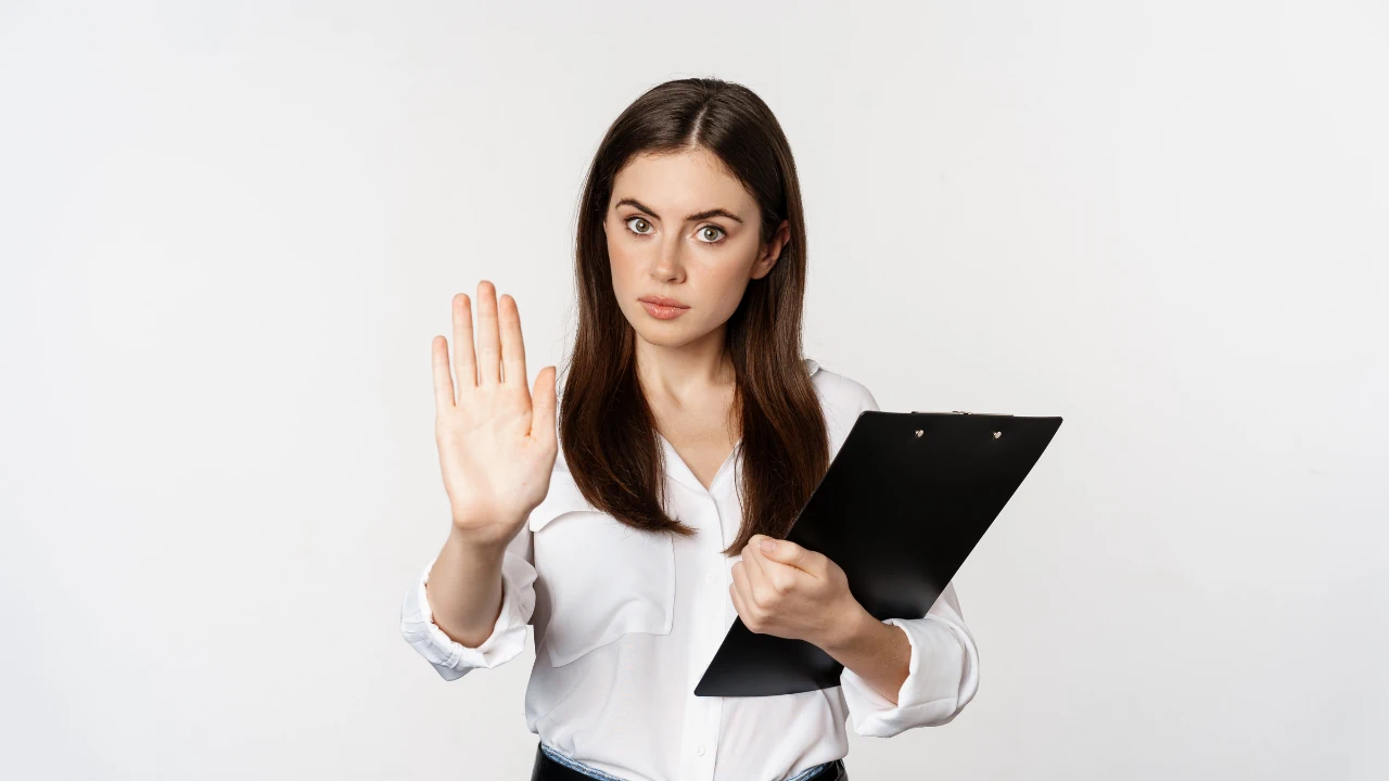 Professional woman holding a clipboard and raising her hand in a warning gesture, symbolising bookkeeping red flags.