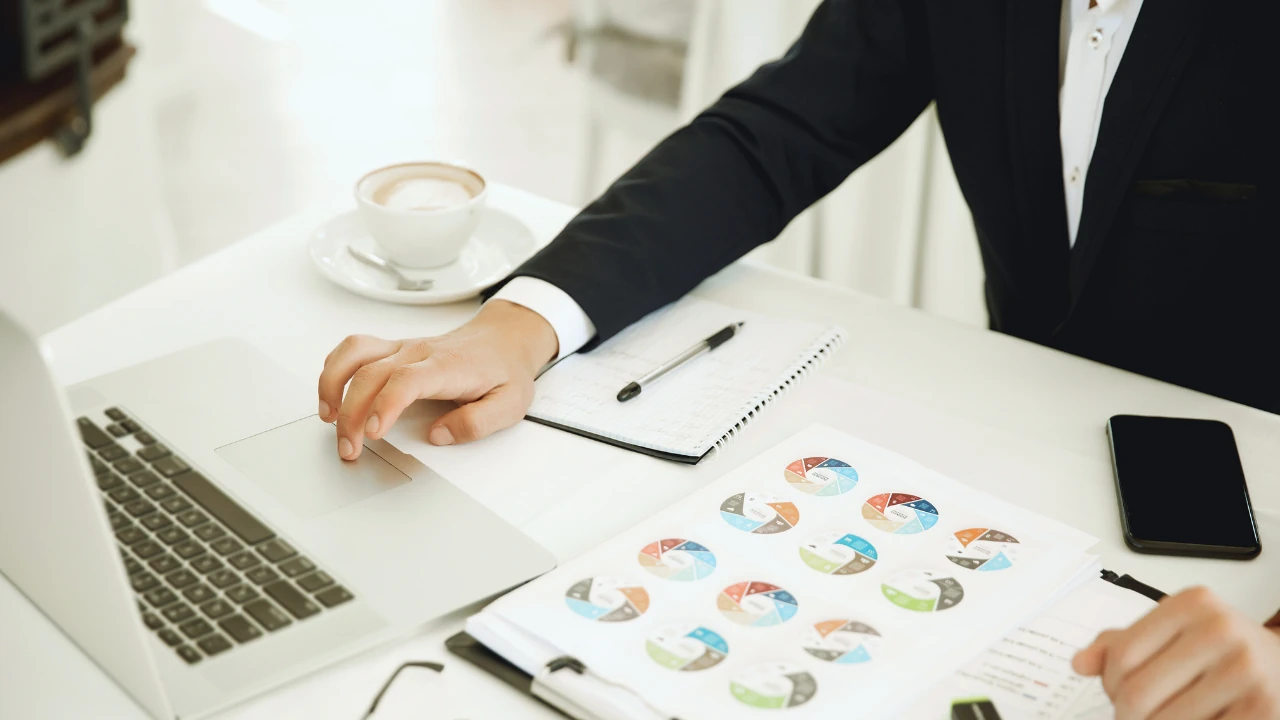  Business professional using a laptop with financial charts and client guides for business finance on the desk