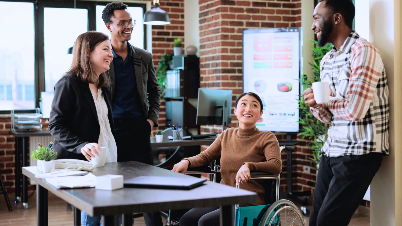 Diverse colleagues, including a team member in a wheelchair, collaborating in a modern office, representing Inclusion and Accessibility Statement.