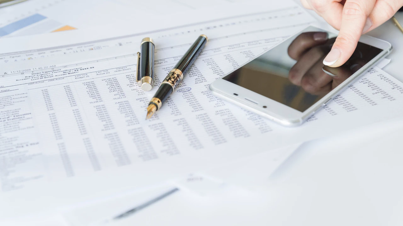Person using a smartphone on top of financial spreadsheets and documents, representing Terms of Service.