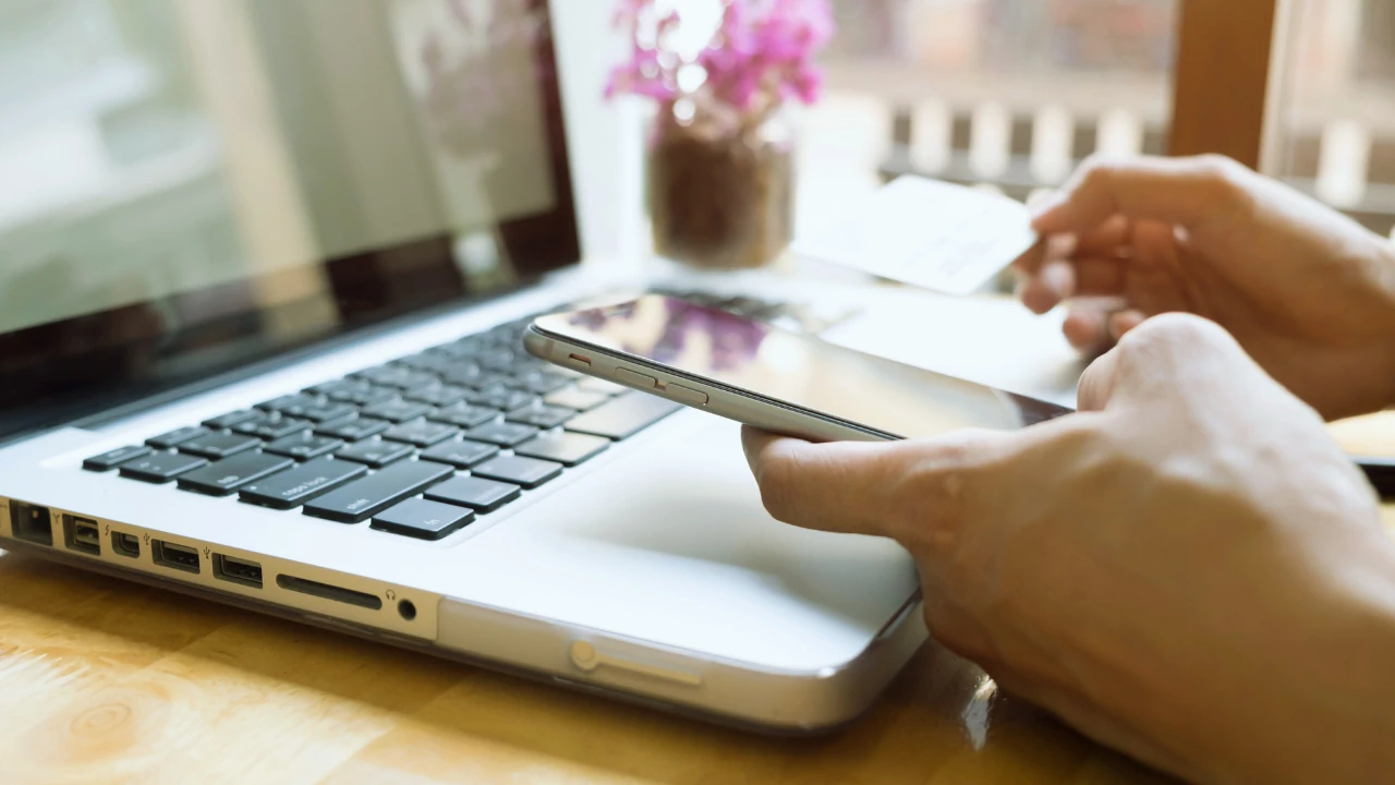 Business owner using phone and laptop to manage finances, related to paying yourself as a director Ireland