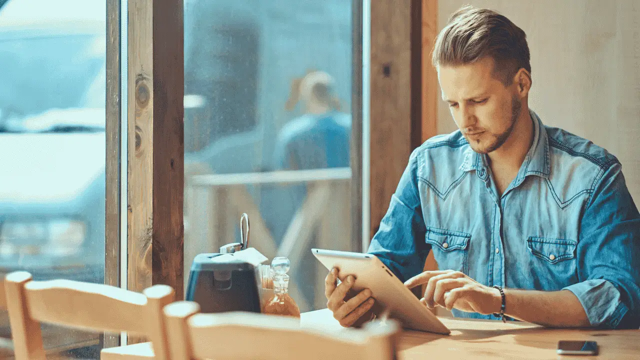 Entrepreneur reading on a tablet in a cafe, exploring insights from The Myth of Normal about wellbeing and business balance.