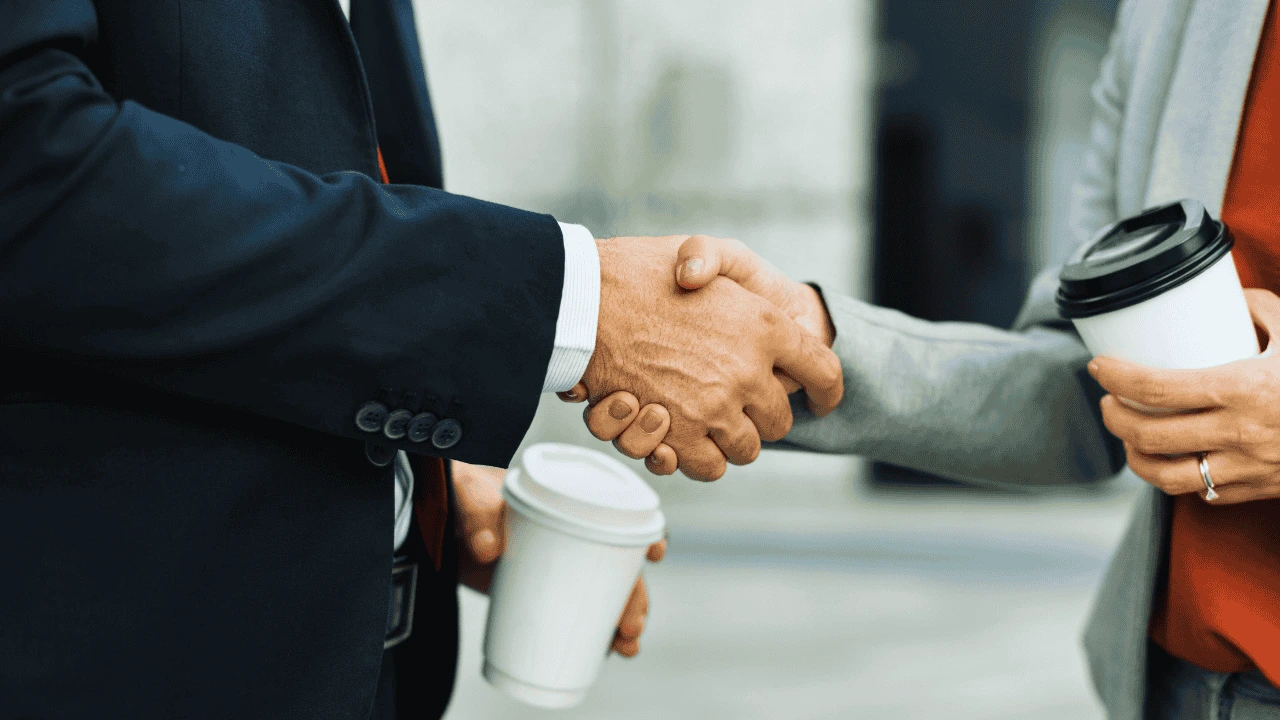 Two corporate professionals shaking hands over coffee, symbolizing personal branding lessons for corporate professionals.