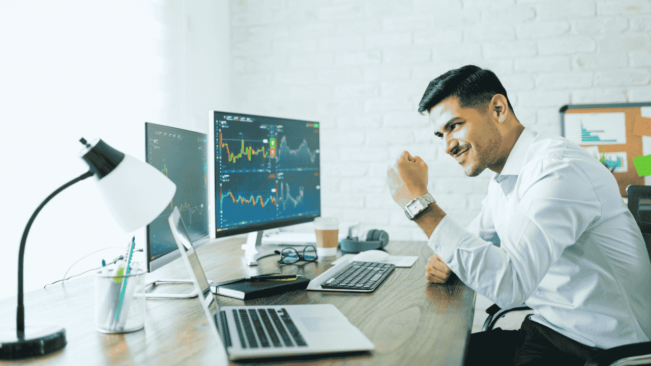 Business owner celebrating financial success at desk with multiple monitors, symbolizing simple accounting for startups.