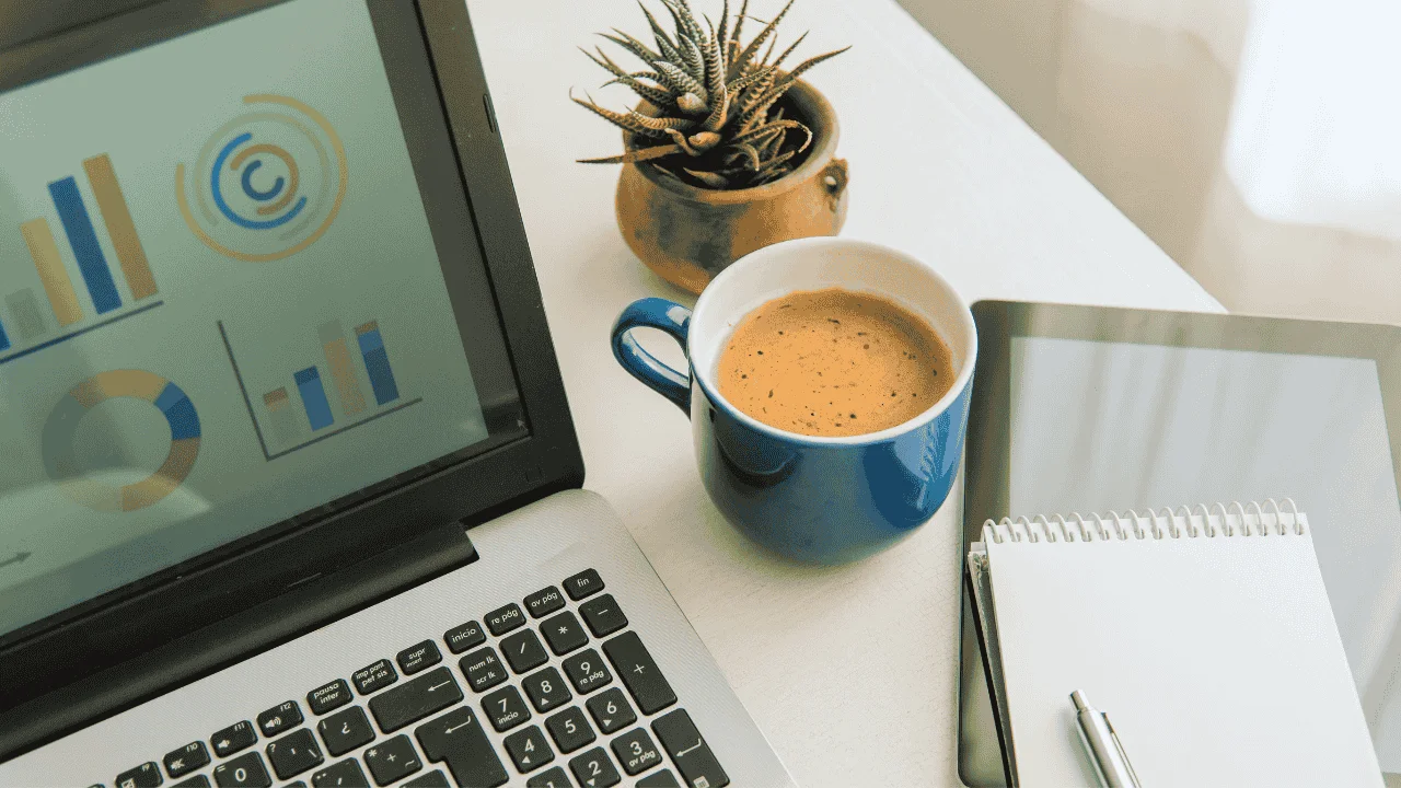 Laptop with financial charts, coffee cup, and notebook — symbolizing financial systems for small business.