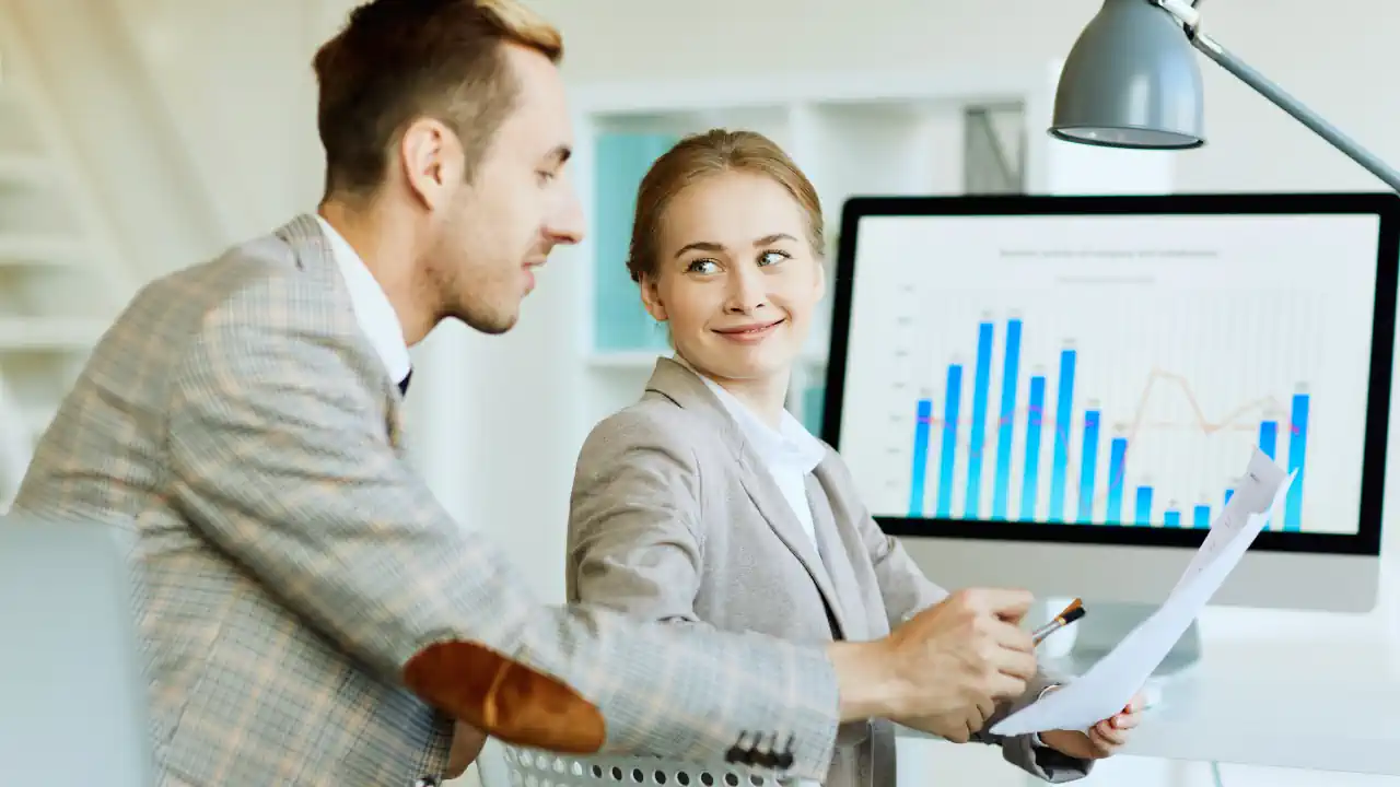 Two business professionals reviewing financial charts on a computer screen, illustrating the benefits of Profit First for small business owners.